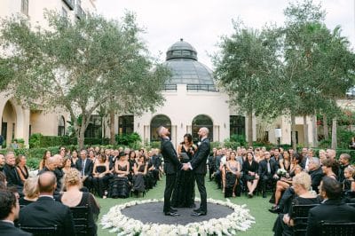 wedding officiant & two grooms in the center of the lawn, wedding guests dressed in all black surrounding the grooms, Orlando, FL