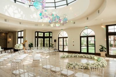 ballroom set for a wedding ceremony, chairs in a circular arrangement with white floral bunches in a semi circle at the front of the room, Orlando, FL