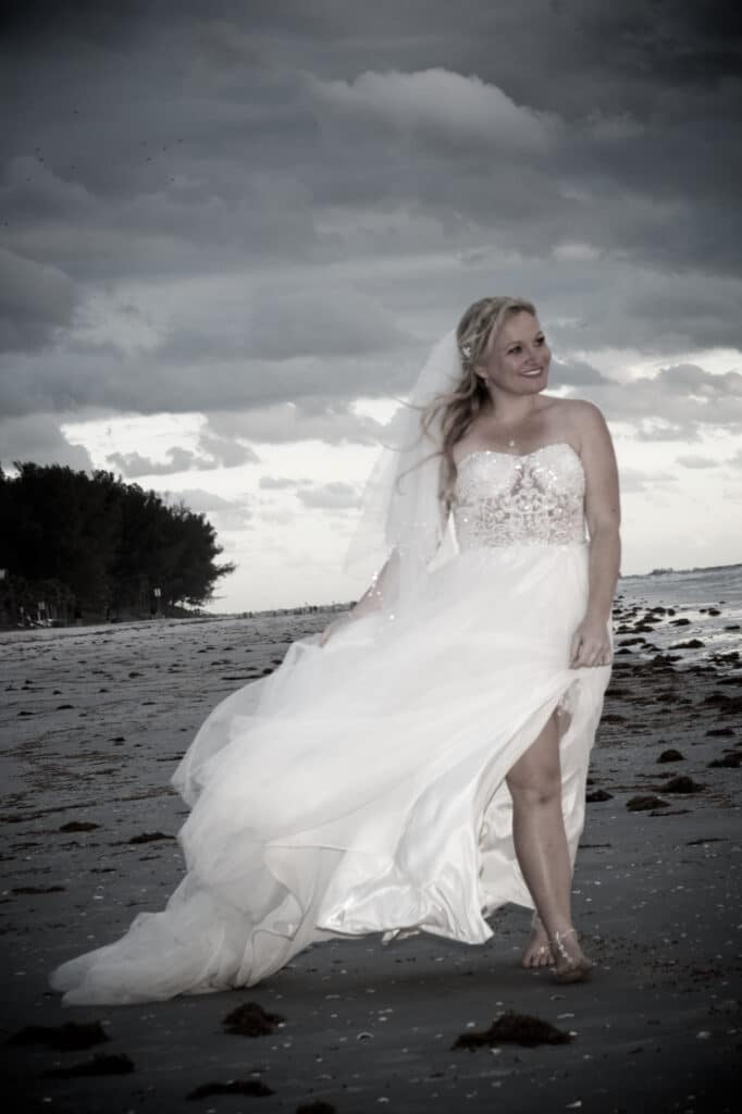 black and white photo of a bride walking along a beach, grey sky and clouds, Orlando, FL