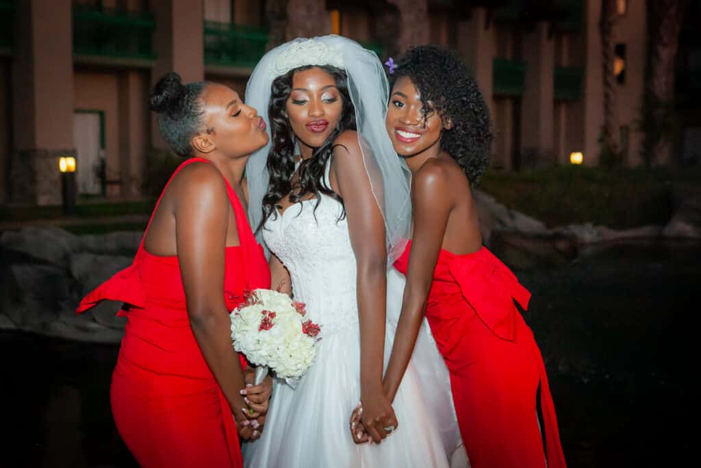 bride in her wedding gown, standing with her two bridesmaids, wearing red dresses, white bouquet with hints of red, Dream Day Digital, Orlando, FL