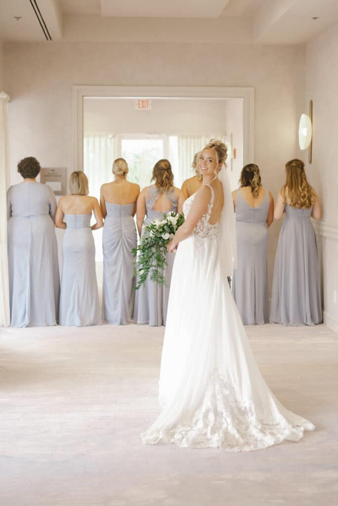 bride standing behind her bridesmaids as they look out a window, bride turns back to the camera, showing off her bouquet, Dream Day Digital, Orlando, FL