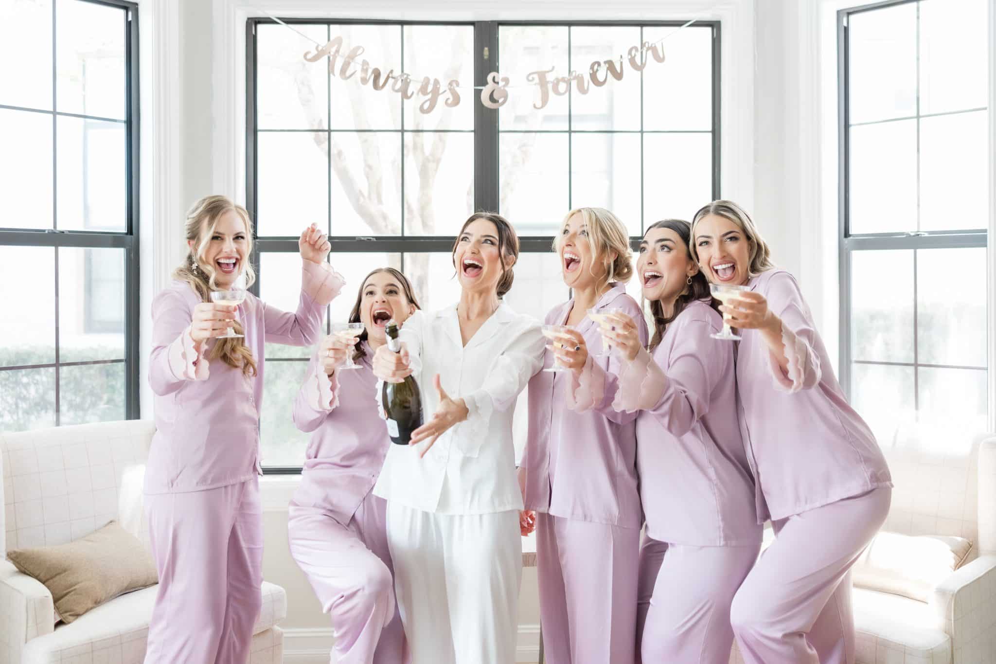 bride with bridal party in matching light purple pajamas in a bright white get ready room