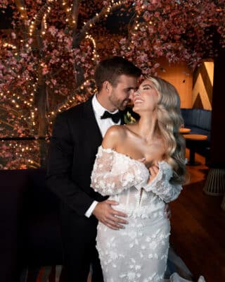 Bride and groom share a romantic moment at Lake Nona Wave Hotel in Orlando Florida, surrounded by pink cherry blossom floral installations and warm string lights, bride wearing an off-the-shoulder floral applique gown