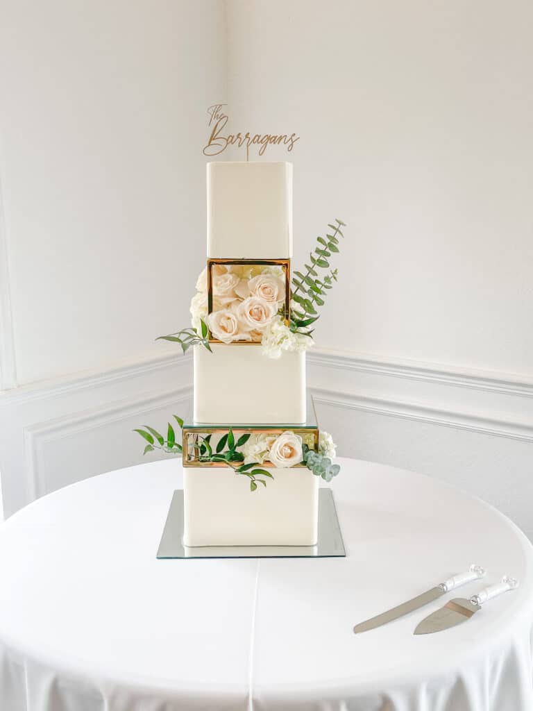 three tiered white cake, square shape, flowers on the side, cake servers on the table, name of the couple on top, Orlando, FL