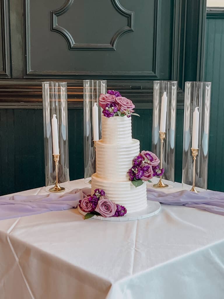 three tiered cake, purple flowers on each layer, white tablecloth with a purple runner, candles lit behind, Orlando, FL