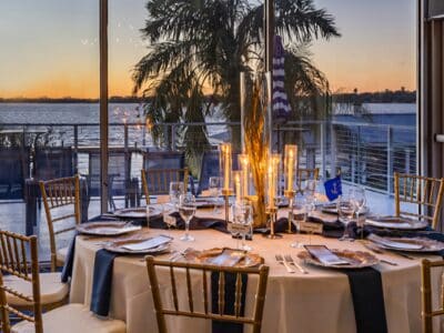 outdoor dining table, palm tree, ocean and sunset in the background, candles lit on the table, white tablecloth, blue napkins, patio dining, Mount Dora Yacht Club, Orlando, FL