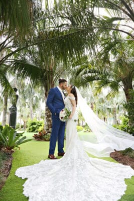 bride and groom kissing on the lawn, palm trees, wading gown train and veil spread out, beautiful day, Orlando, FL