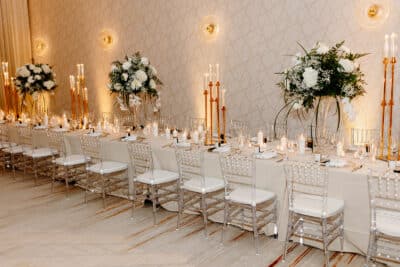 zoomed out view of the long table, set for dinner, white tablecloth, tall white taper candles in holders, large white floral centerpieces, white plates with gold trim, white napkins, white round candles and tea light candles on table, Lake Nona Wave Hotel, Orlando, FL
