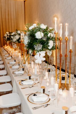 long table set for dinner, white tablecloth, tall white taper candles in holders, large white floral centerpieces, white plates with gold trim, white napkins, white round candles and tea light candles on table, Lake Nona Wave Hotel, Orlando, FL
