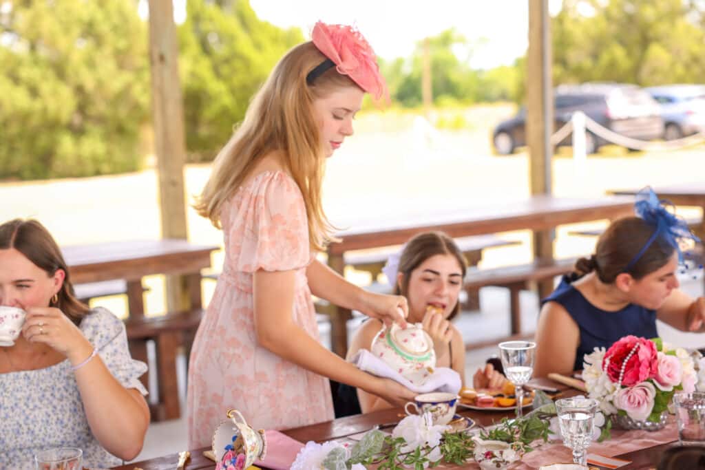 young woman in a pink dress and pink hat pouring her tea and tea for her neighbor, Houses of Windsor, Orlando, FL