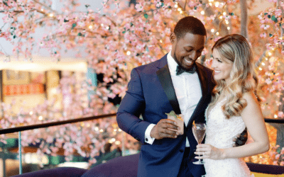 Bride and groom share a romantic moment holding champagne glasses in front of illuminated pink cherry blossom trees at Lake Nona Wave Hotel in Orlando Florida
