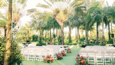 outdoor wedding ceremony, palm trees, white chairs in rows with a center aisle, flowers at the feet of the chairs on the inside of the aisle, Orlando, FL