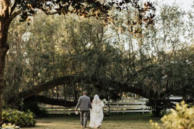 bride and groom walking in the distance towards large trees, clear day, outdoors, Orlando, FL