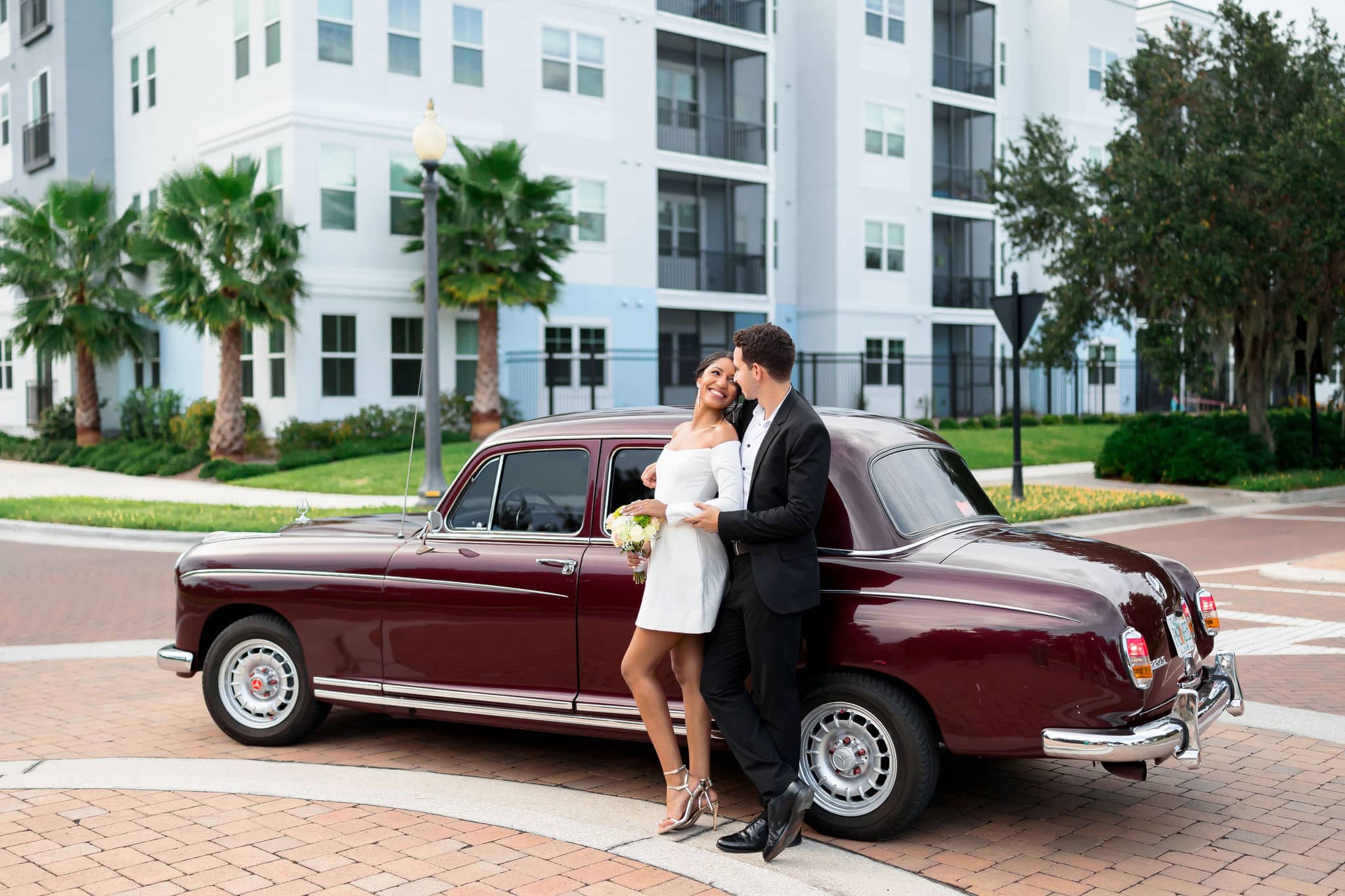 bride and groom celebrating their timeless and chic wedding in front of a Burgundy classic car 