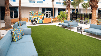 Bright outdoor courtyard at Aloft Orlando Lake Nona wedding venue featuring lush artificial turf lawn, blue lounge seating with colorful pillows, palm trees, and a vibrant painted food truck in the background, Lake Nona Orlando Florida