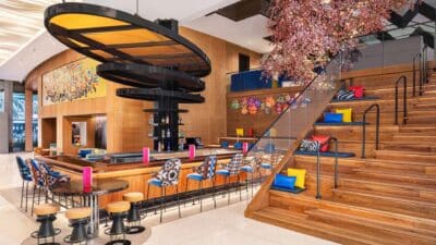 Colorful and modern hotel lobby bar with wood-paneled walls, decorative cherry blossom tree, vibrant seating, and grand staircase at Lake Nona Wave Hotel in Orlando Florida, a luxury wedding venue in Central Florida