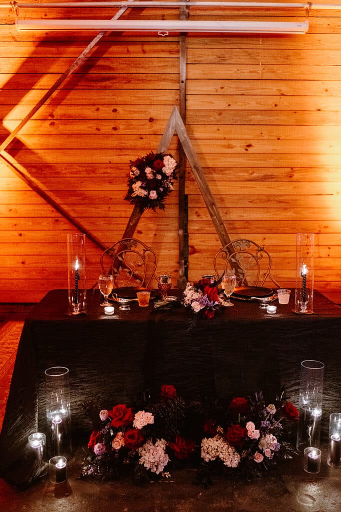 sweatheart table with dark and moody decor and floral with a beautiful arch in the back 