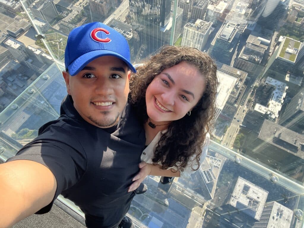 Selfie of a couple posing with a clear floor that has an amazing view of the city underneath them. 