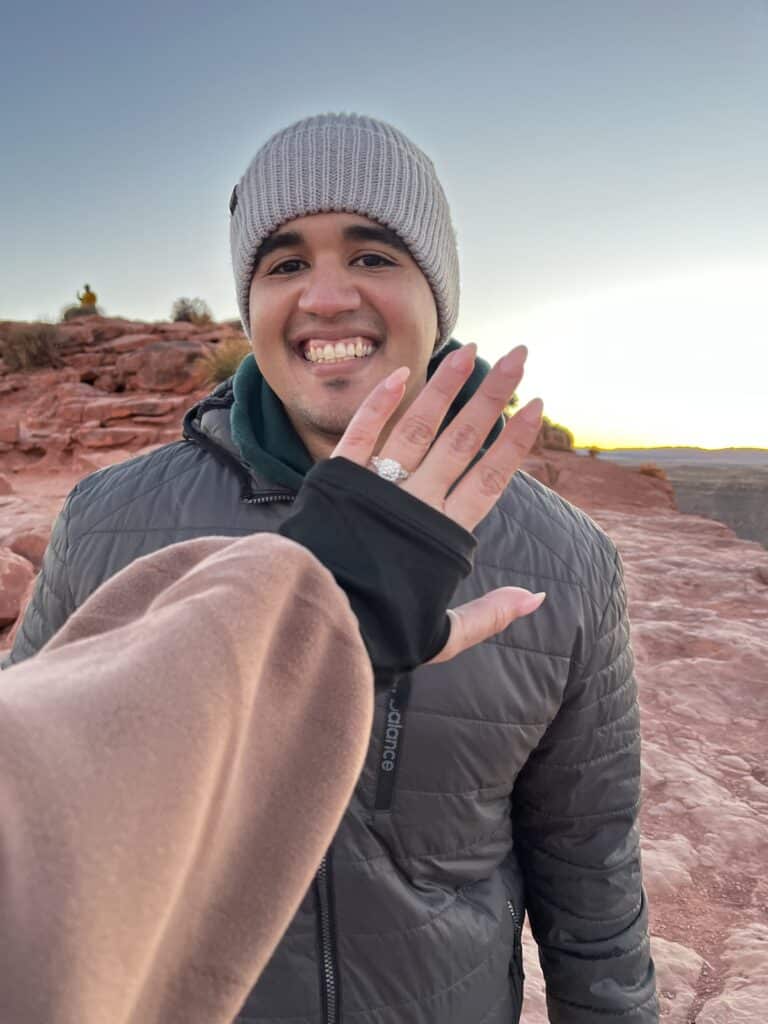 Fiance showing off her engagement ring with her hand in front of her partners face with the grand canyon in the background. 