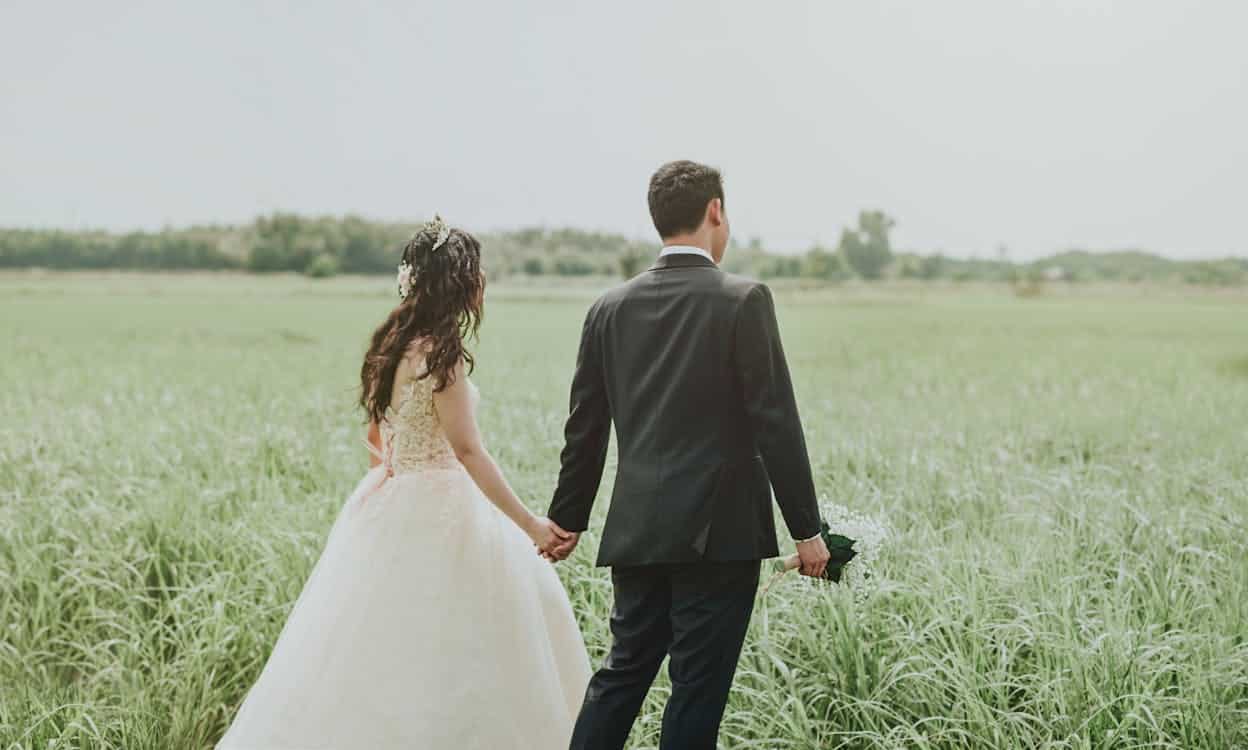 bride and groom holding hands in a green field