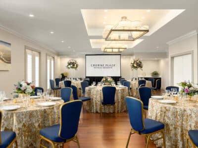 large meeting space, set for a dinner reception, large round tables, blue chairs, gold and tan tablecloths with a textured design, large screen at the front of the room, Orlando, FL