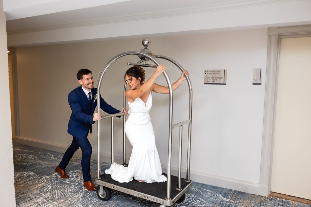 Groom pushing a hotel cart with the bride on board, through the hotel hallway, Crowne Plaza Orlando Downtown, Orlando, FL
