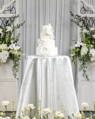 wedding cake on display, three layers, high top table with a silver tablecloth, surrounded by white flowers, Orlando, FL