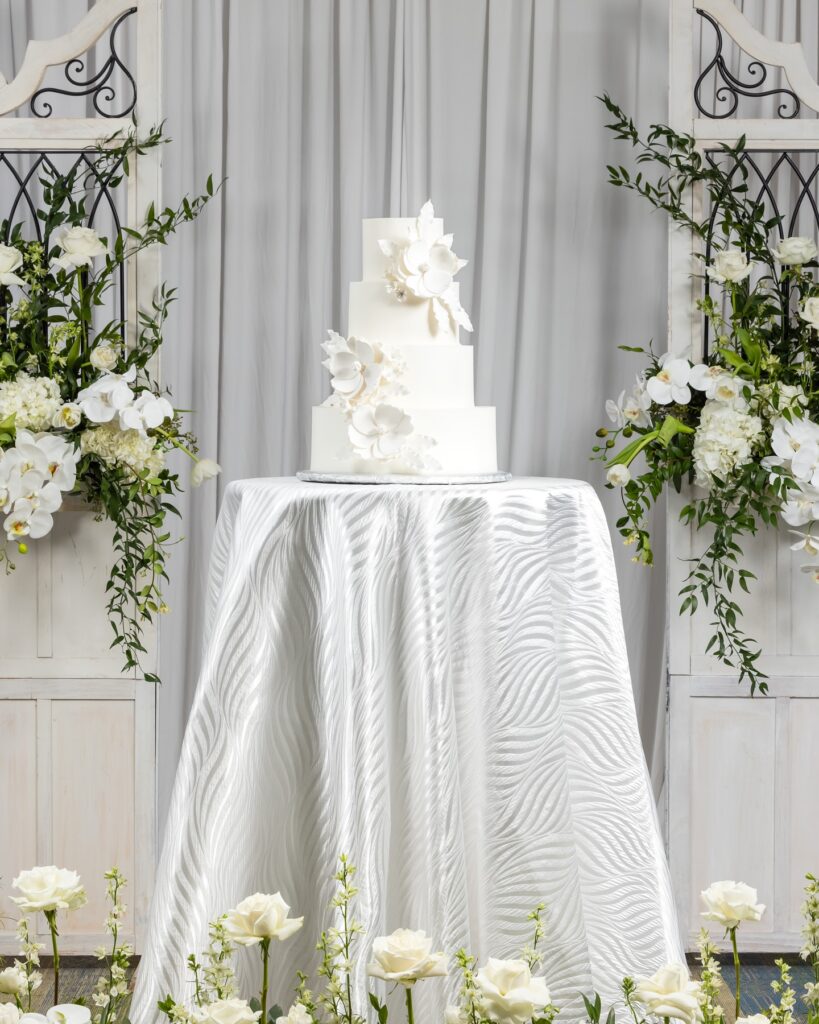 wedding cake on display, three layers, high top table with a silver tablecloth, surrounded by white flowers, Orlando, FL