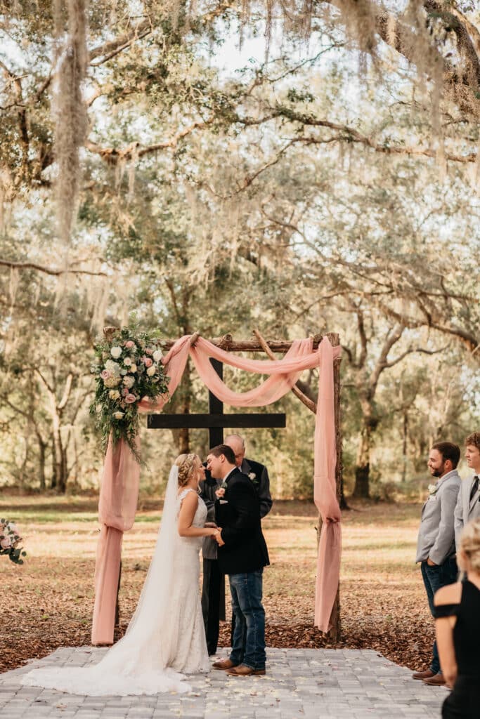 Bride and groom at the altar, outdoors, wooden pergola, tall trees, weeping willows, Legacy at Oak Meadows, Orlando, FL