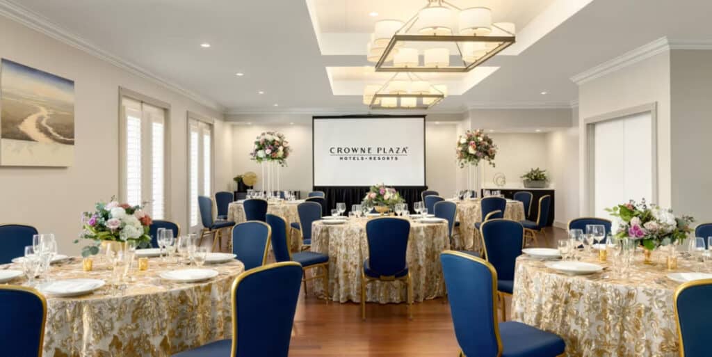 large meeting space, set for a dinner reception, large round tables, blue chairs, gold and tan tablecloths with a textured design, large screen at the front of the room, Orlando, FL