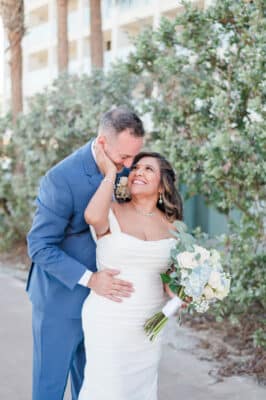 bride looking up at her groom, her hand on his face, his hand on her waist, greenery around them, H Hawkins Photography, Orlando, FL