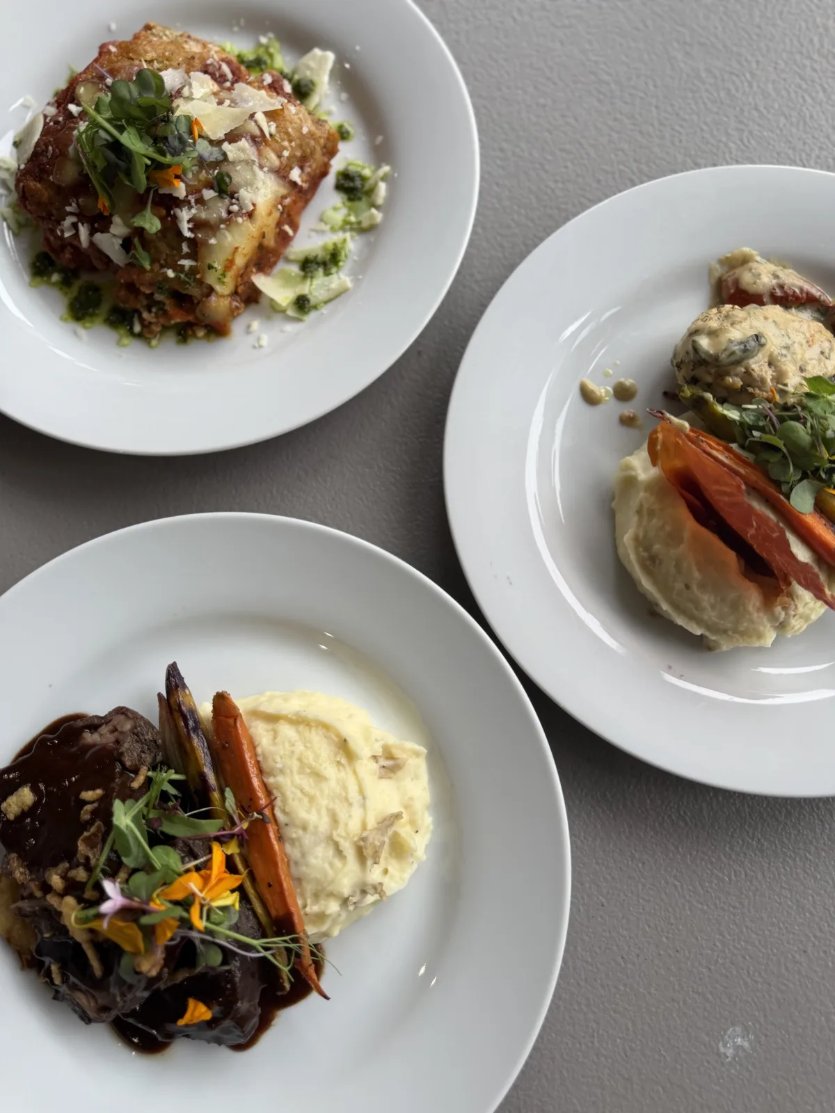 Three gourmet plated wedding entrées by Done Wright Culinary Services featuring herb cream chicken, vegetarian lasagna, and braised beef short ribs with mashed potatoes and seasonal vegetables.