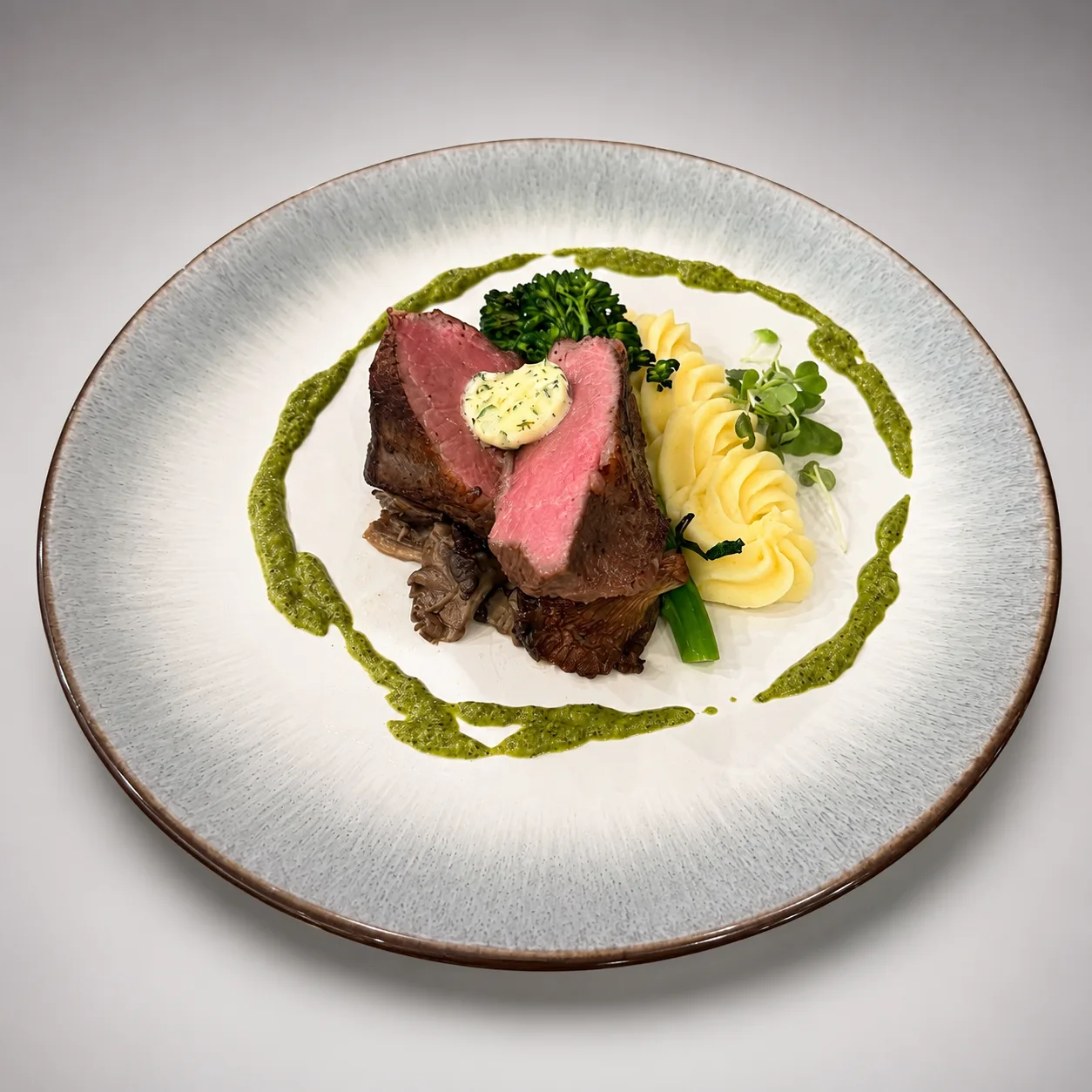 Medium-rare beef tenderloin with herb butter, whipped potatoes, broccolini, mushrooms, and herb sauce, elegantly plated by Done Wright Culinary Services.