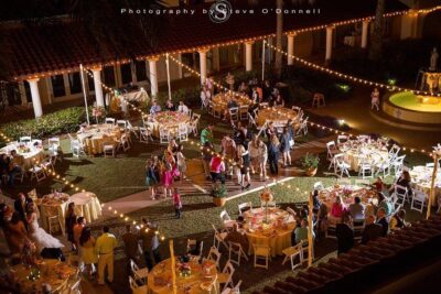 Aerial evening view of an elegant outdoor wedding reception at Mission Resort and Club in Central Florida, featuring round dining tables with warm candlelight, string lights, and lush courtyard grounds in a Mediterranean-inspired setting