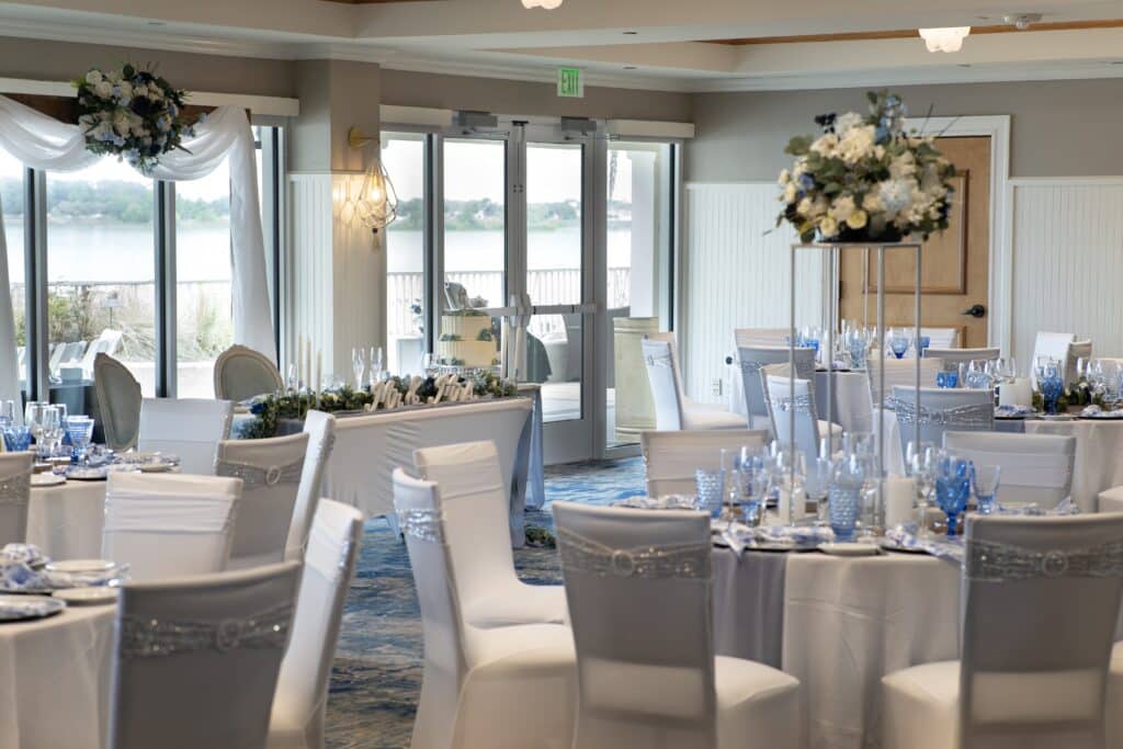 wedding reception, tall floral centerpieces of white flowers, tall windows, white table cloths with silver runners, white chair covers, accents of blue, The Waterfront Inn, Orlando, FL