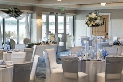 wedding reception, tall floral centerpieces of white flowers, tall windows, white table cloths with silver runners, white chair covers, accents of blue, The Waterfront Inn, Orlando, FL