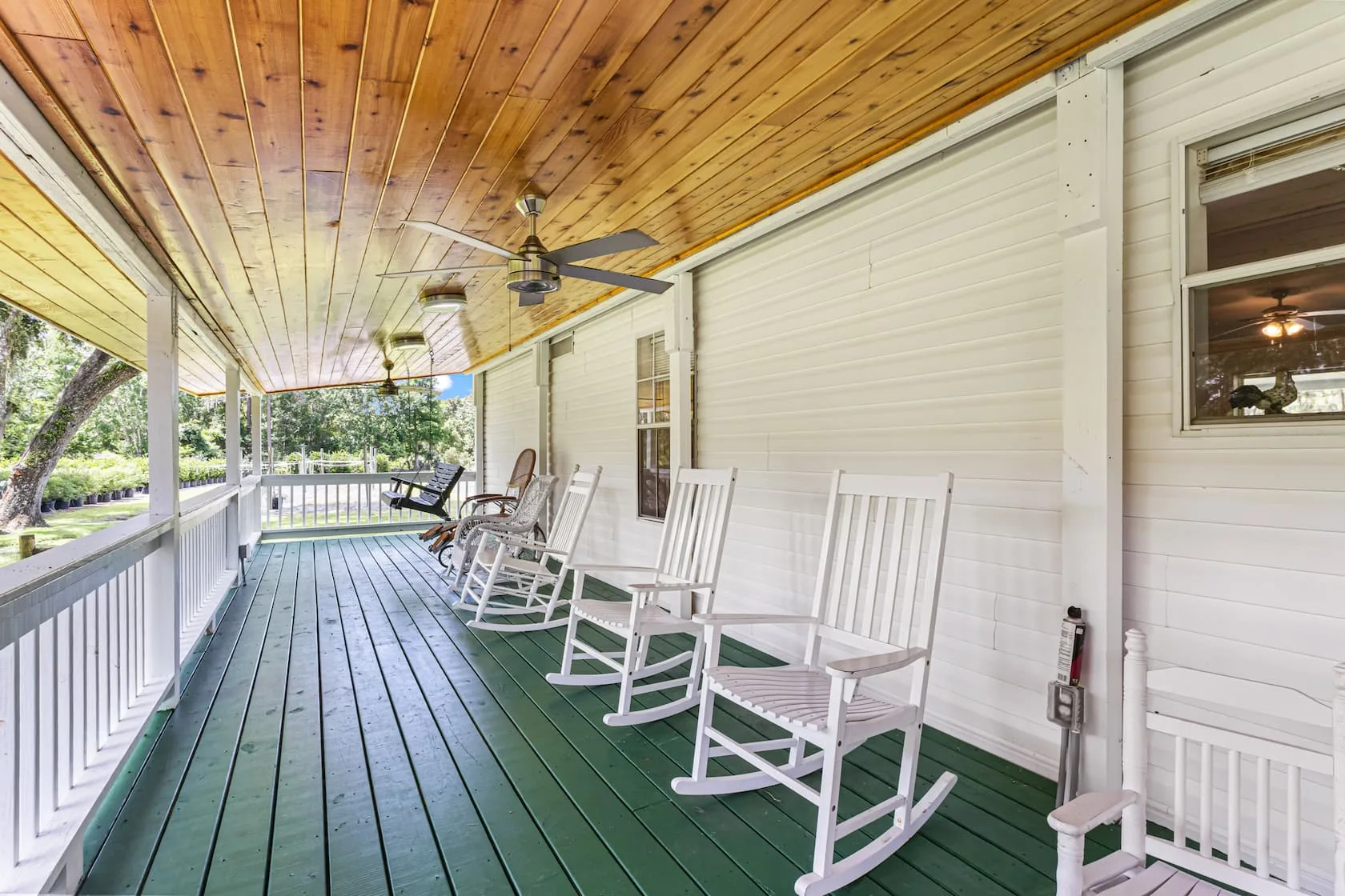 Wide wraparound front porch with green-painted wooden floor, white rocking chairs, wood-plank ceiling, and ceiling fans at Ruby Oaks Events wedding venue in Central Florida