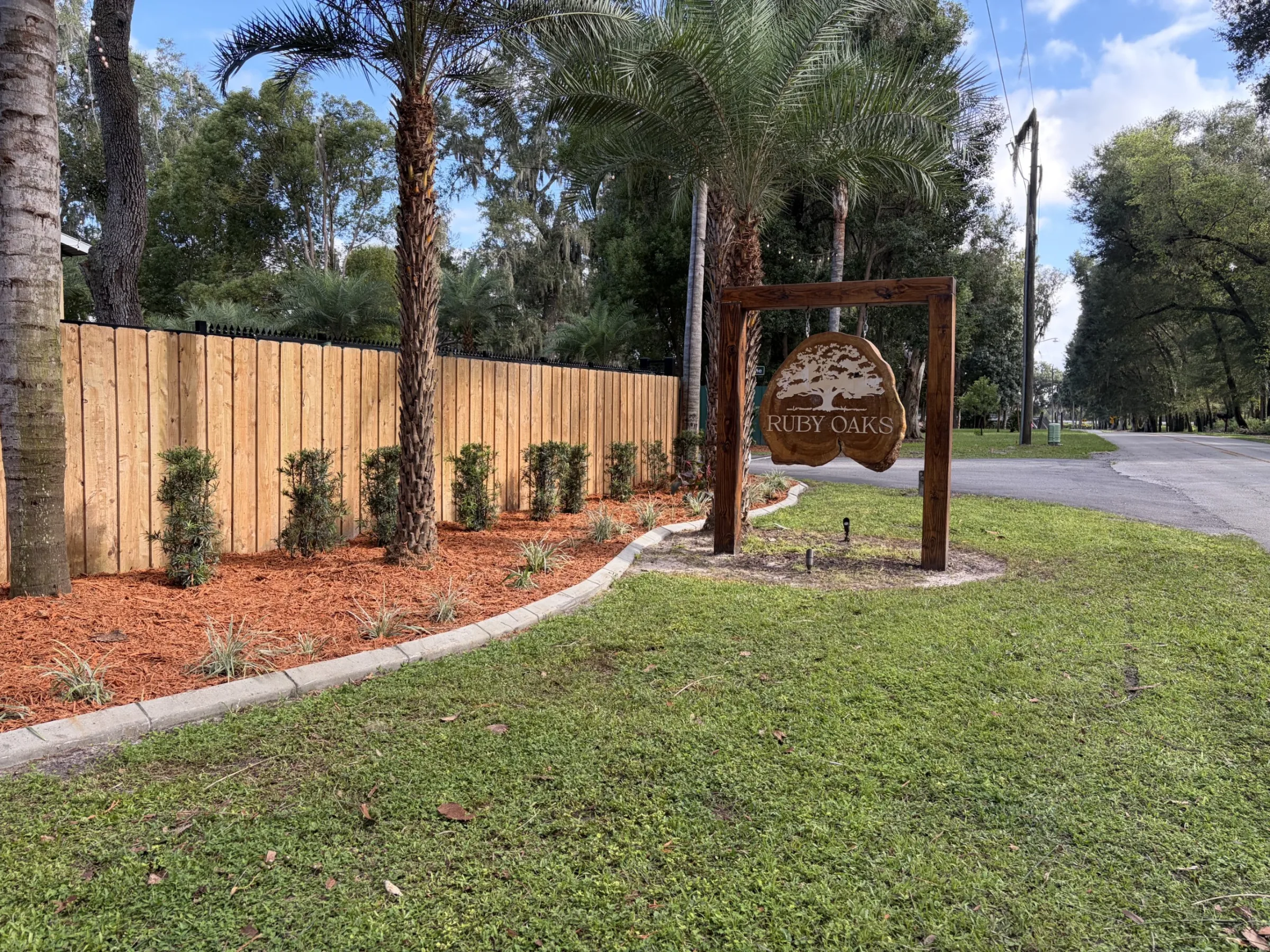 Ruby Oaks Events wedding venue entrance sign with wooden arch, palm trees, fresh wood privacy fence, and manicured landscaping in Central Florida