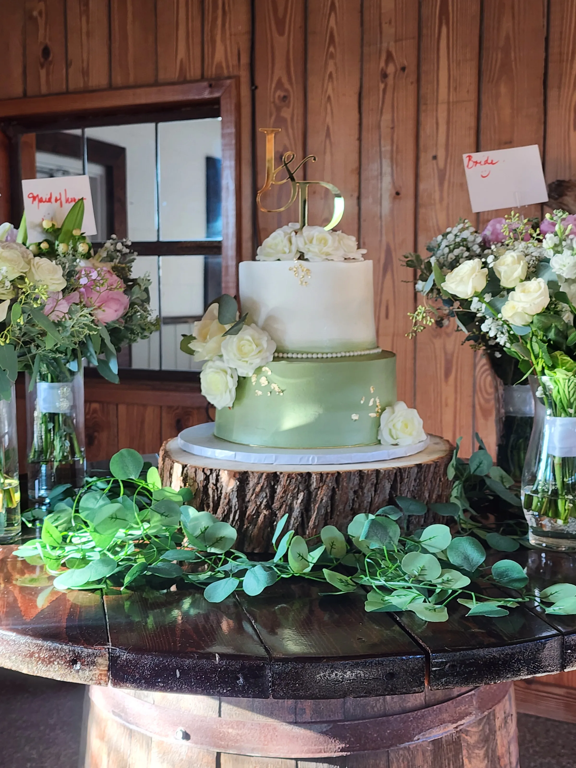 Wedding cake display at The Ranch at St. Cloud on whiskey barrel with wood riser, greenery, and floral arrangements.