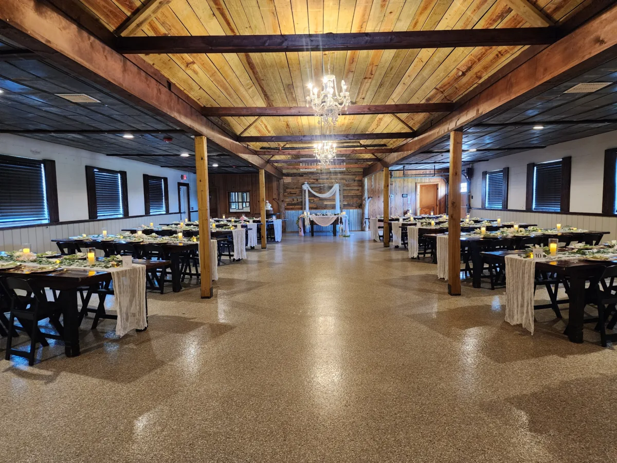 Wide view of decorated reception barn at The Ranch at St. Cloud with farm tables, chandeliers, and draped sweetheart table backdrop.