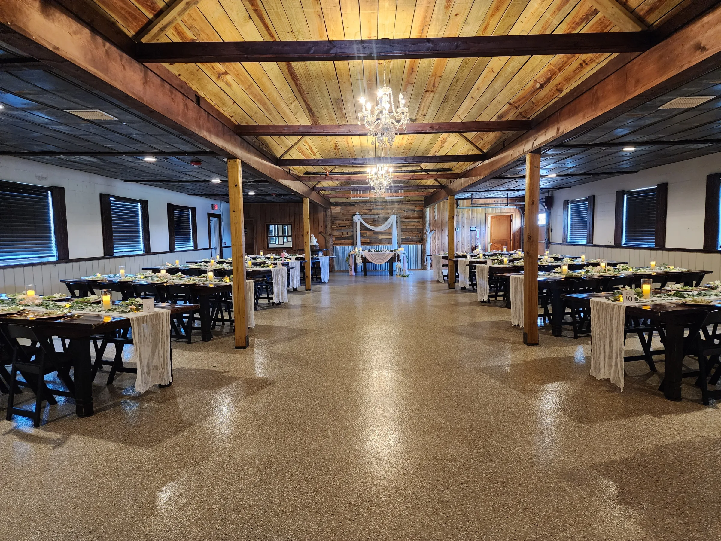 Wide view of decorated reception barn at The Ranch at St. Cloud with farm tables, chandeliers, and draped sweetheart table backdrop.