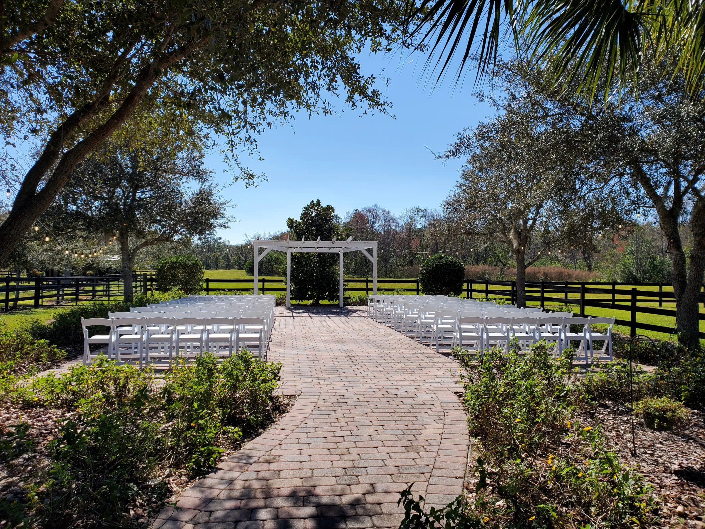 Outdoor wedding ceremony setup at The Ranch at St. Cloud with white chairs, arbor, and brick paver aisle surrounded by trees and greenery.