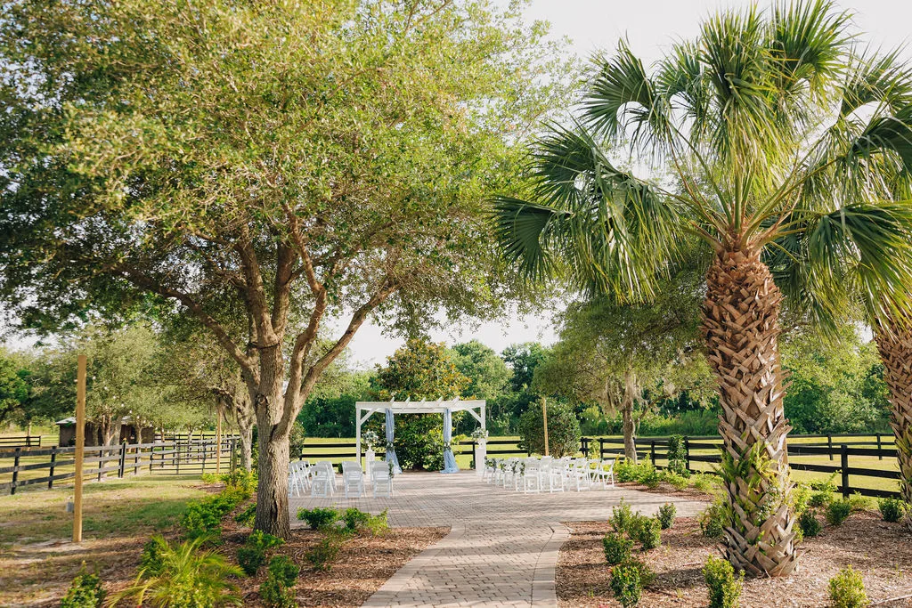 Tree-lined walkway leading to outdoor wedding ceremony at The Ranch at St. Cloud with arbor and white chairs.