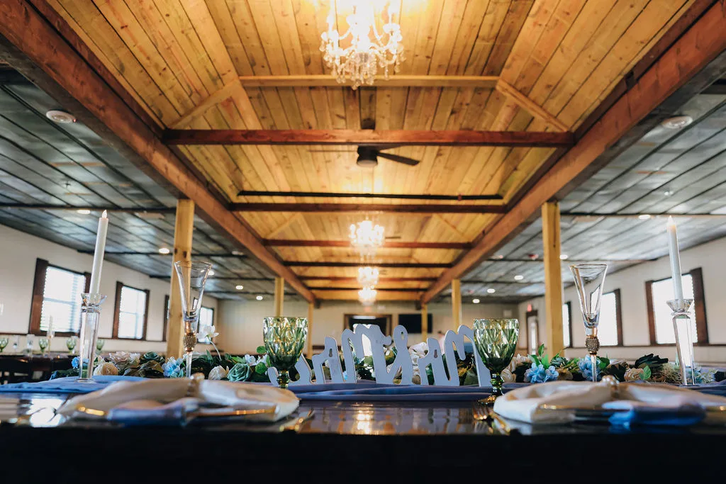 Interior of air-conditioned reception barn at The Ranch at St. Cloud with wood ceilings, chandeliers, and decorated guest tables.