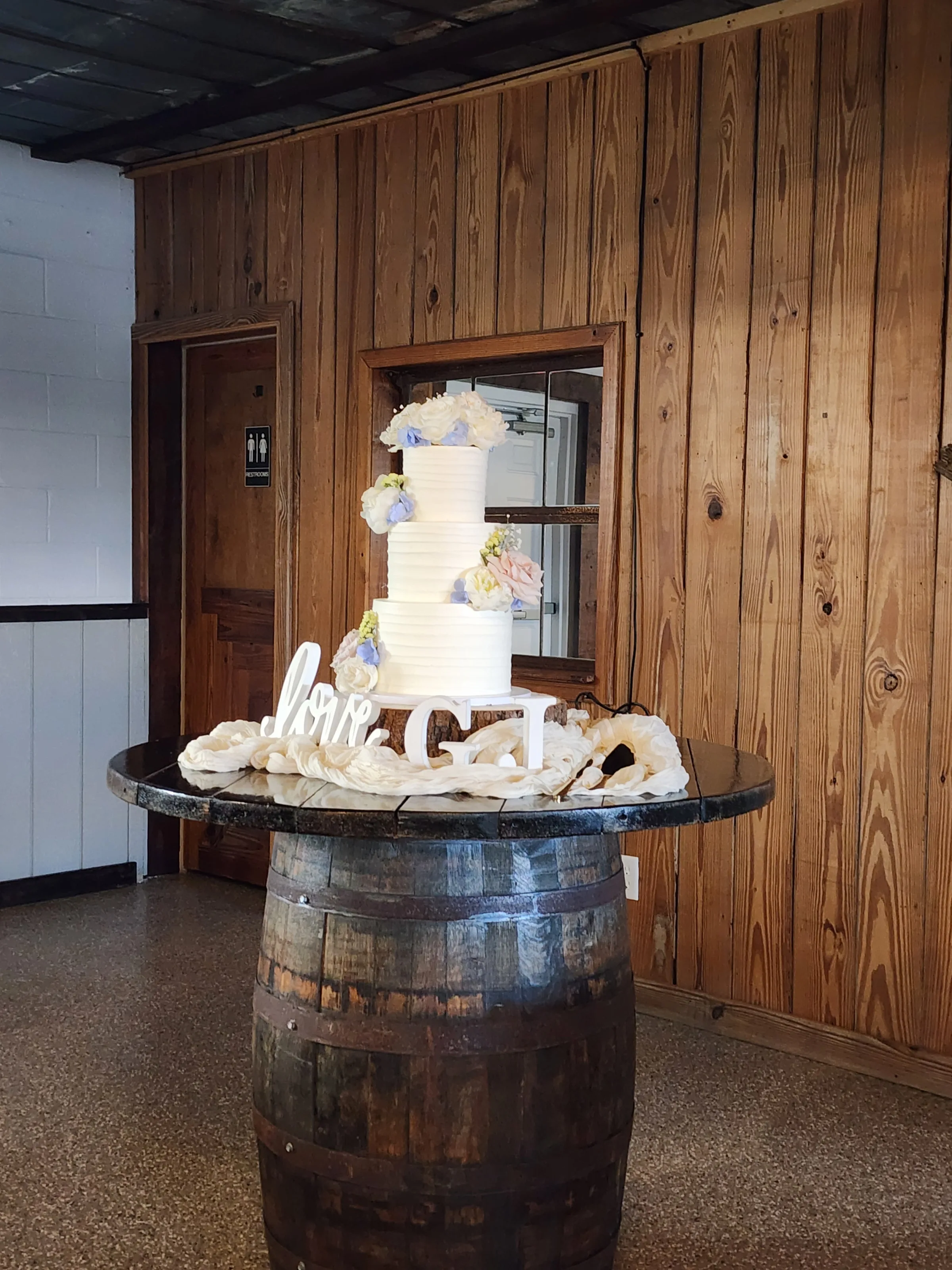 Wedding cake displayed on whiskey barrel table at The Ranch at St. Cloud with wood backdrop and neutral décor.