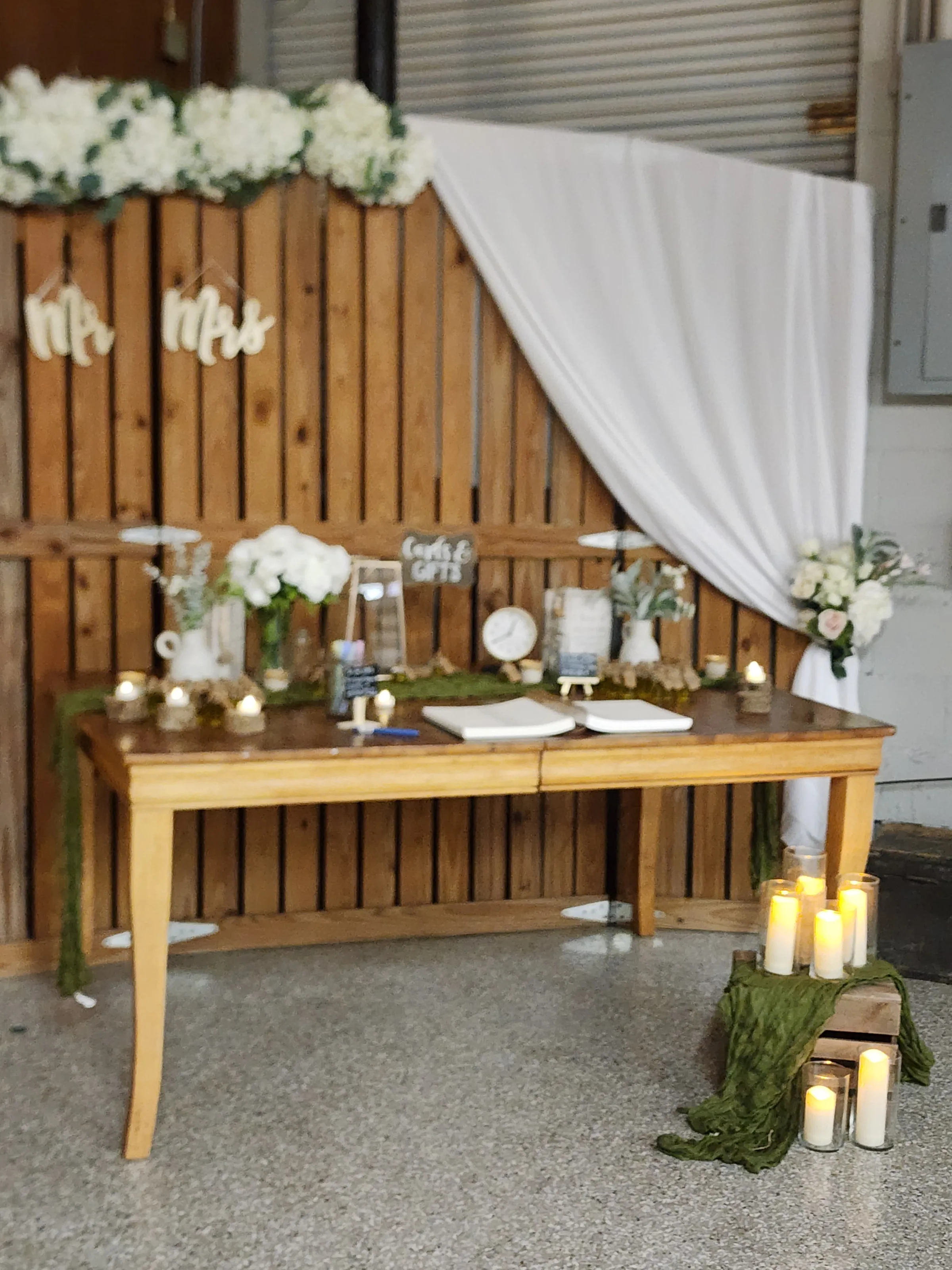 Decorated ceremony table and wood backdrop in Lower Barn at The Ranch at St. Cloud with draping, candles, and floral accents.