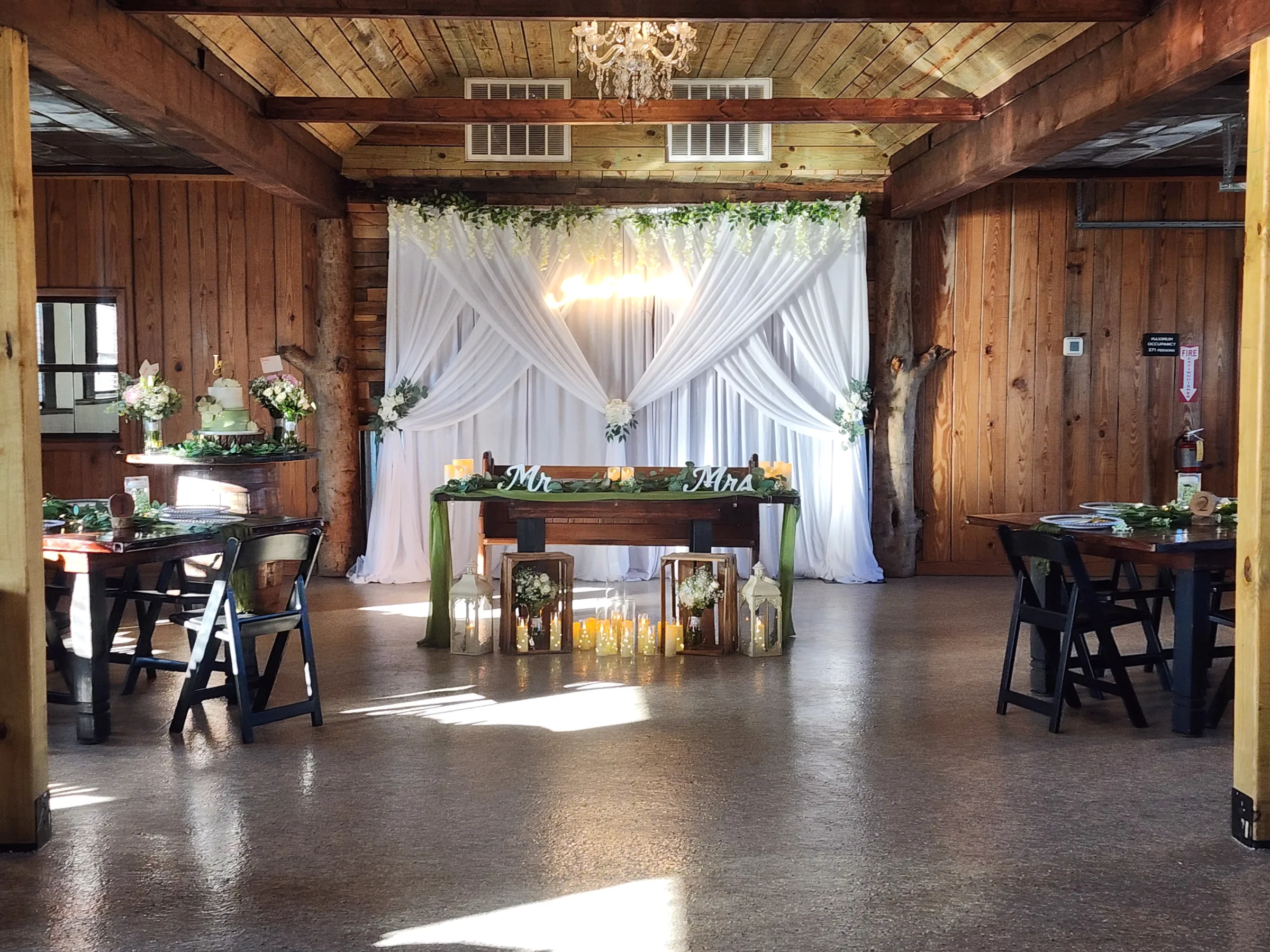 Decorated sweetheart table at The Ranch at St. Cloud with draped backdrop, candles, greenery, and chandelier lighting.