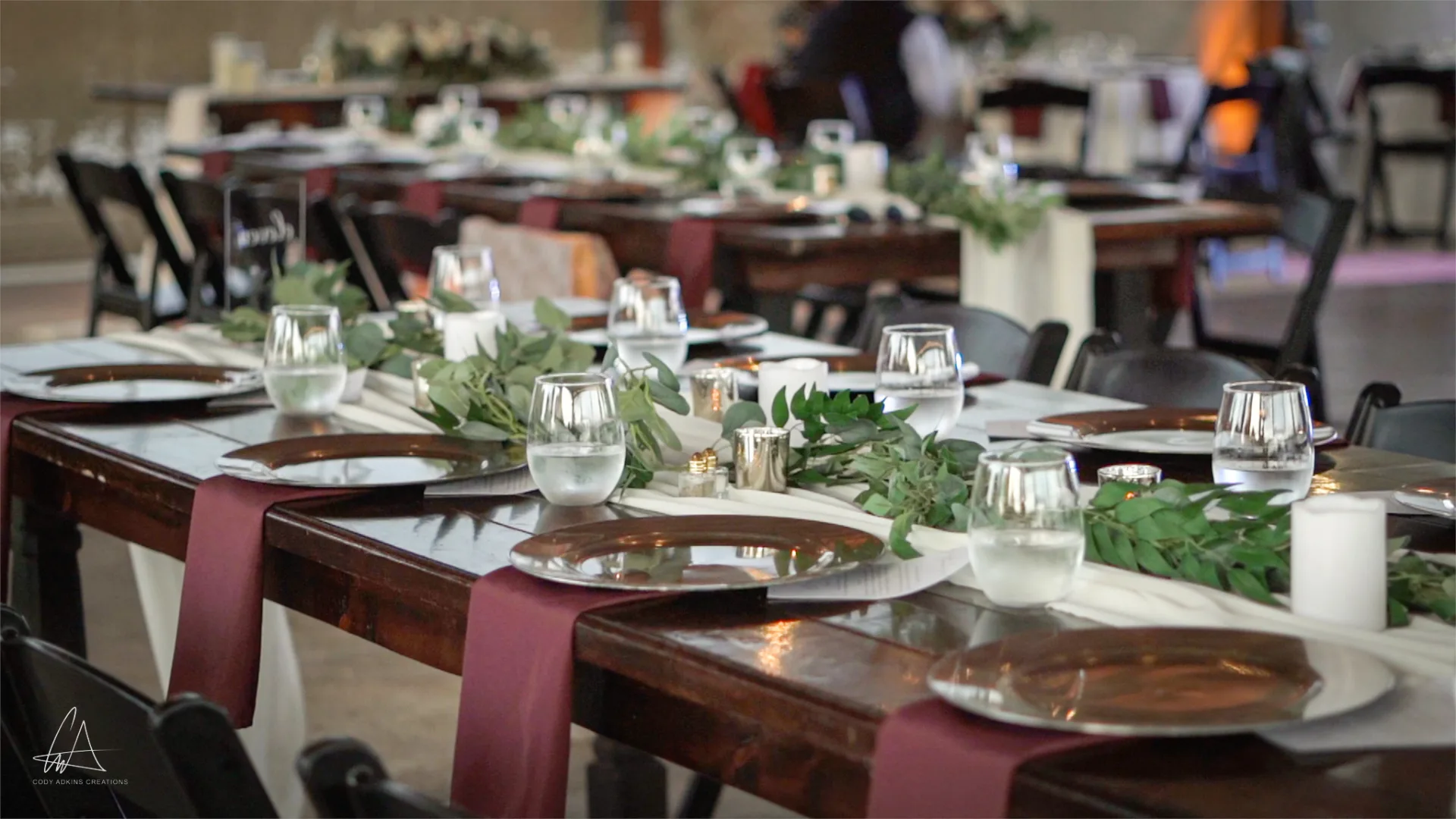 Close-up of wedding reception table at The Ranch at St. Cloud with greenery garland, chargers, glassware, and farm table setting.