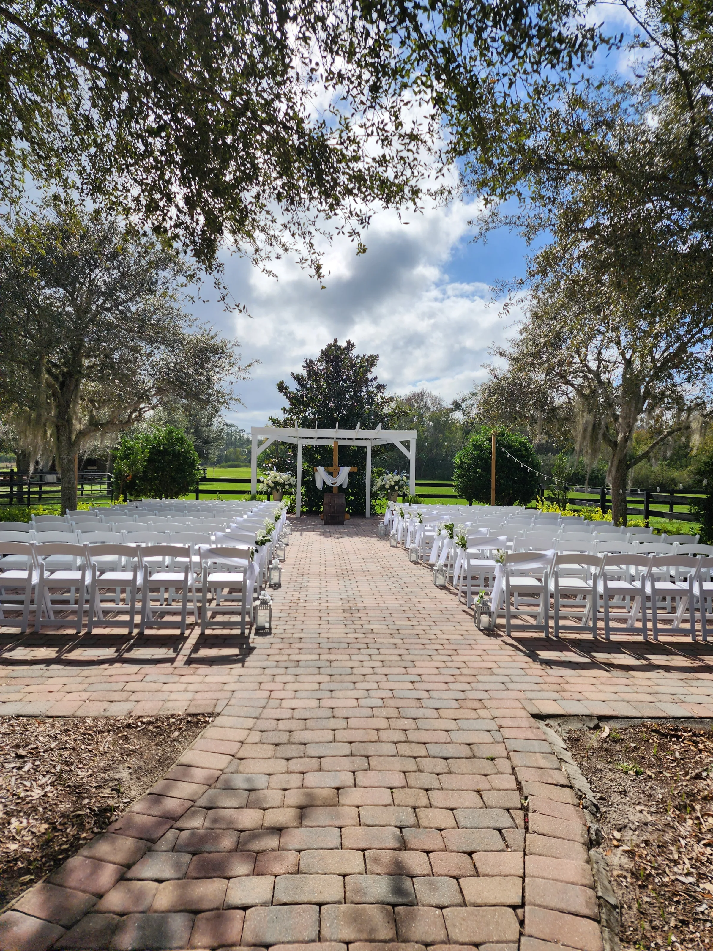 Outdoor wedding ceremony at The Ranch at St. Cloud Paver Area with white chairs, arbor, and brick aisle surrounded by trees.