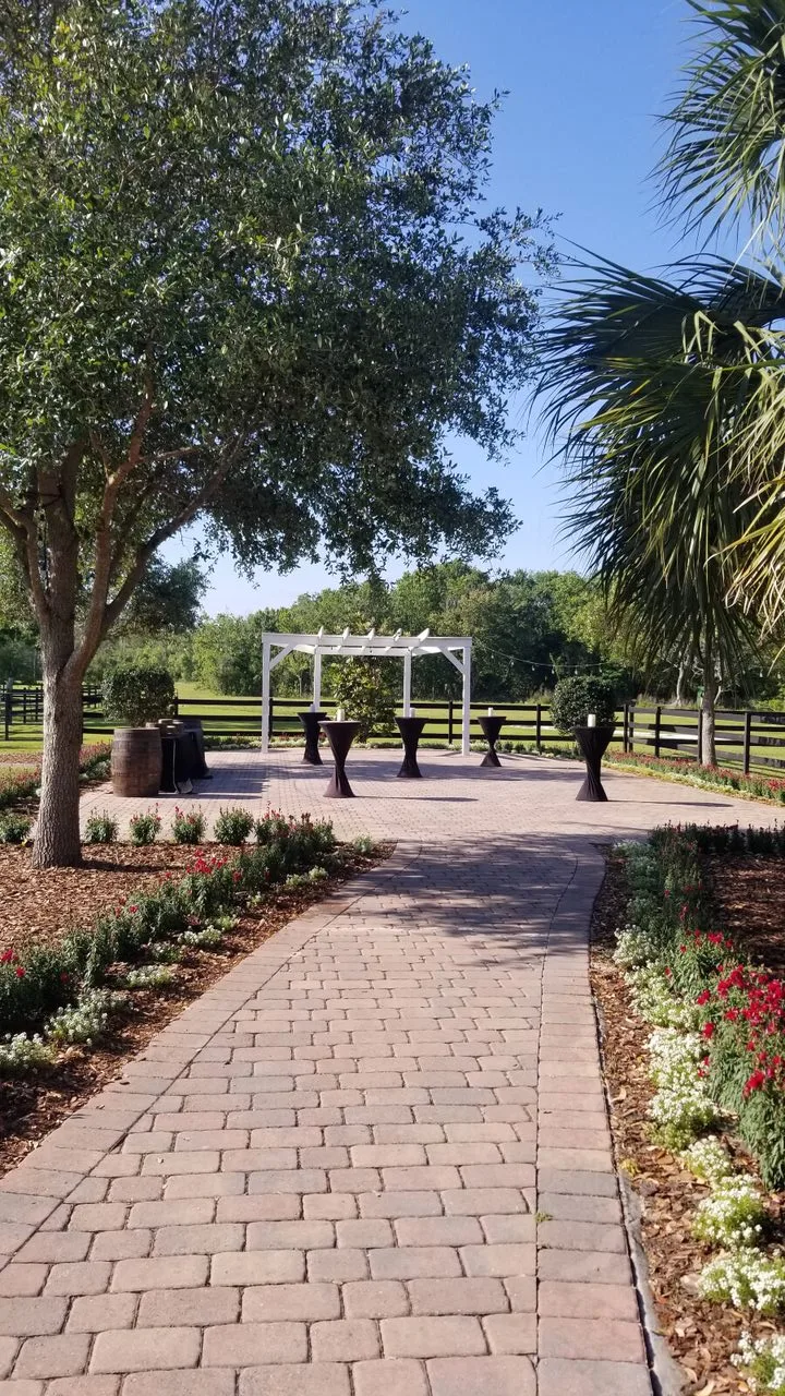 Outdoor cocktail hour setup at The Ranch at St. Cloud Paver Area with high-top tables, arbor backdrop, and landscaped walkway.